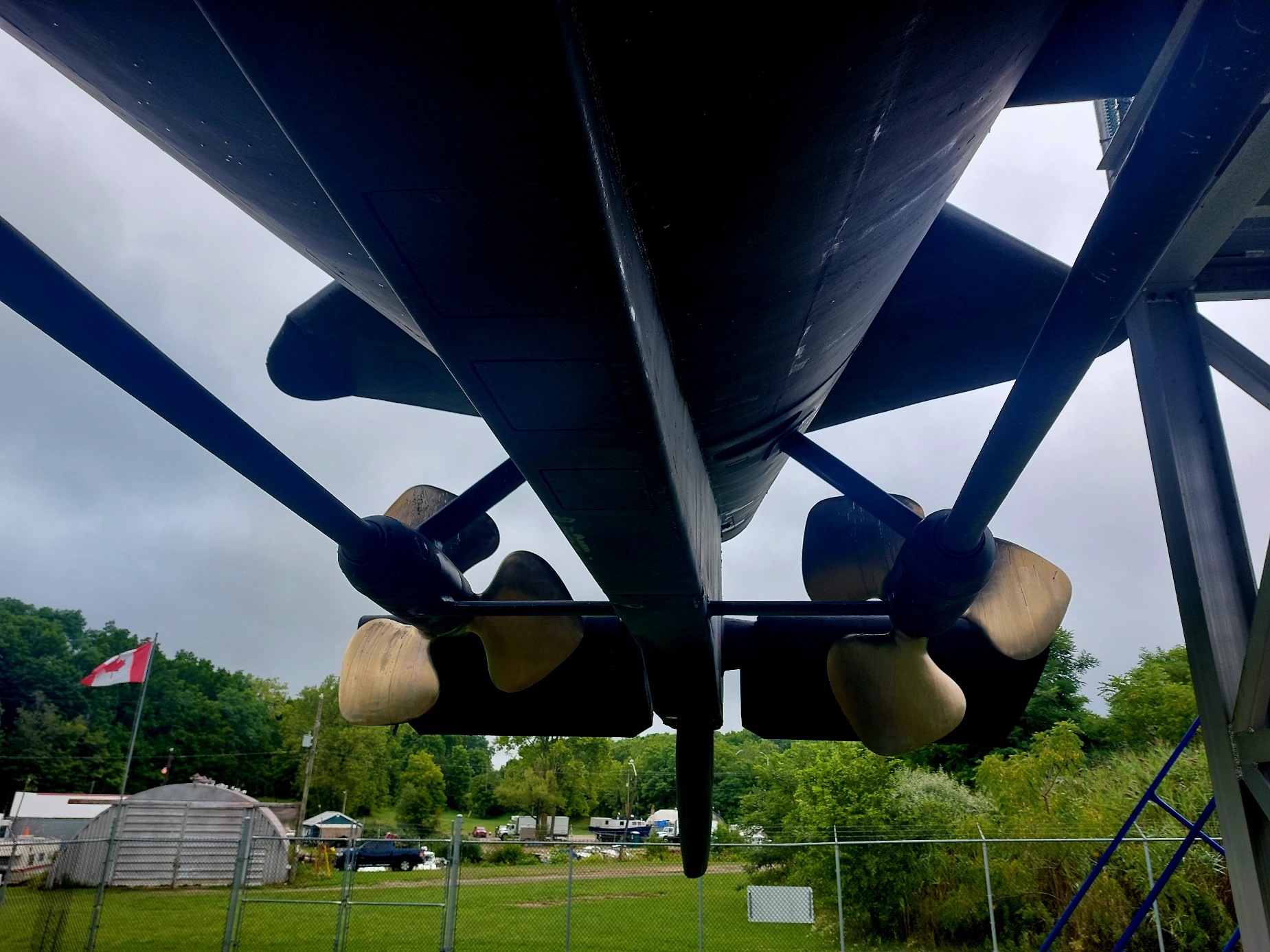 Underneath a cold war submarine looking at the two propellers and a Canadian flag flapping in the wind